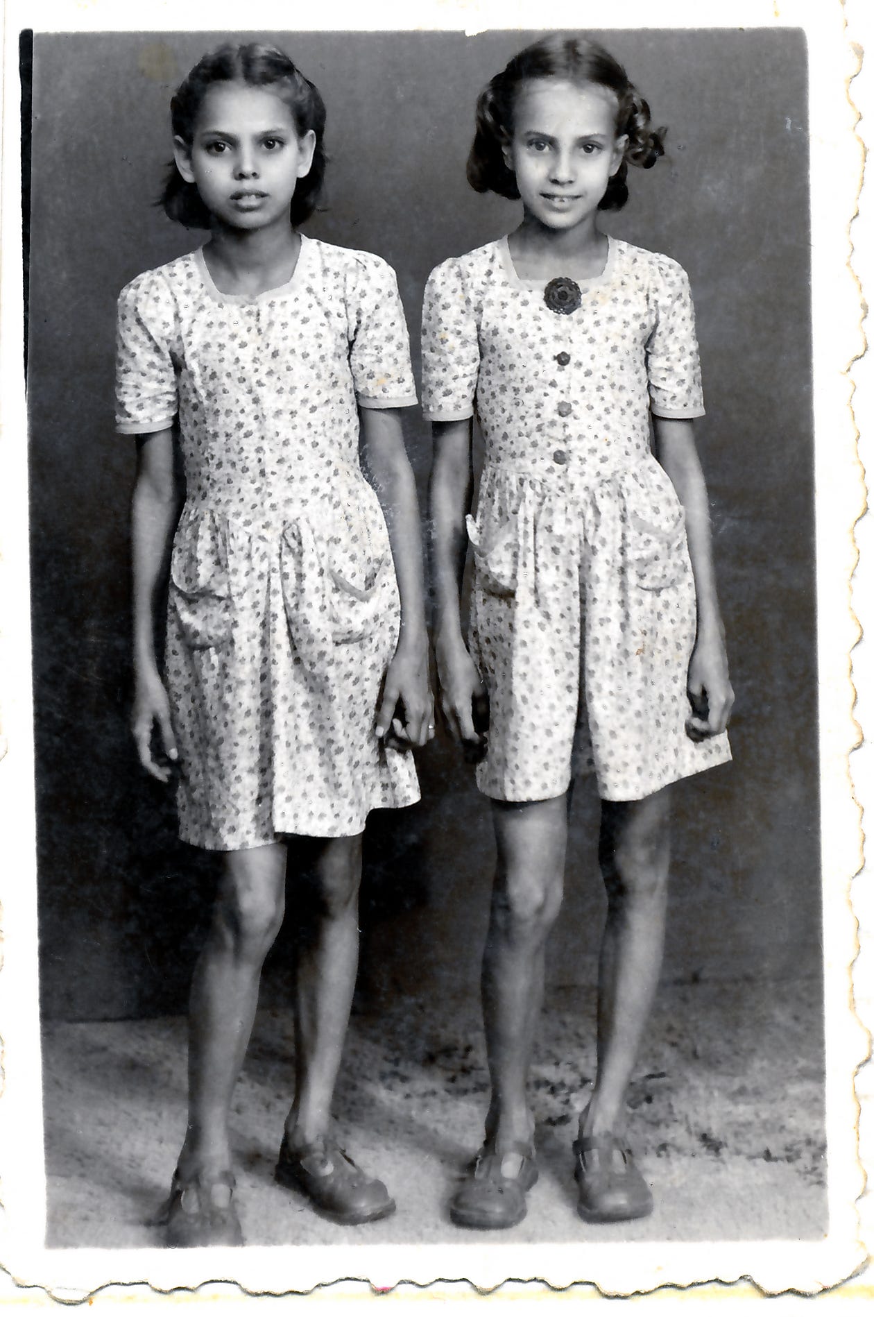 Photo taken in 1948 of two little girls, one solemn, one smiling, dressed in home-made floral print dresses.