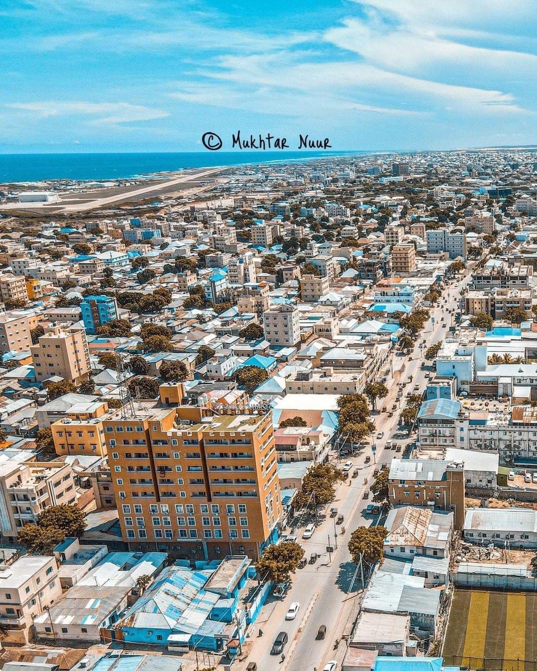 An aerial view of downtown Mogadishu, showing a mix of mid-rise and low-rise buildings, with the sea in the background