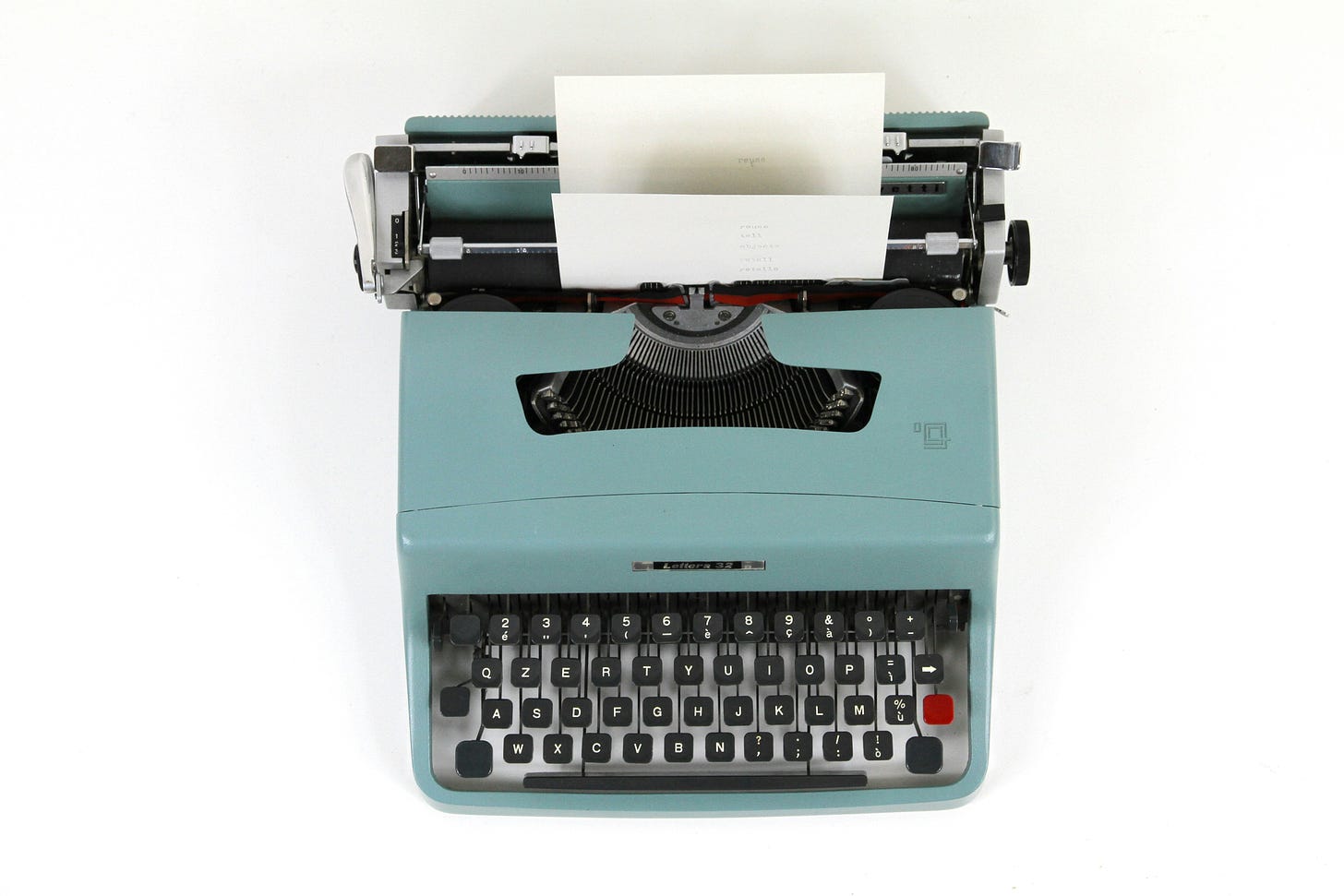 Um máquina de datilografar verde num fundo branco vista de cima, com o papel em branco