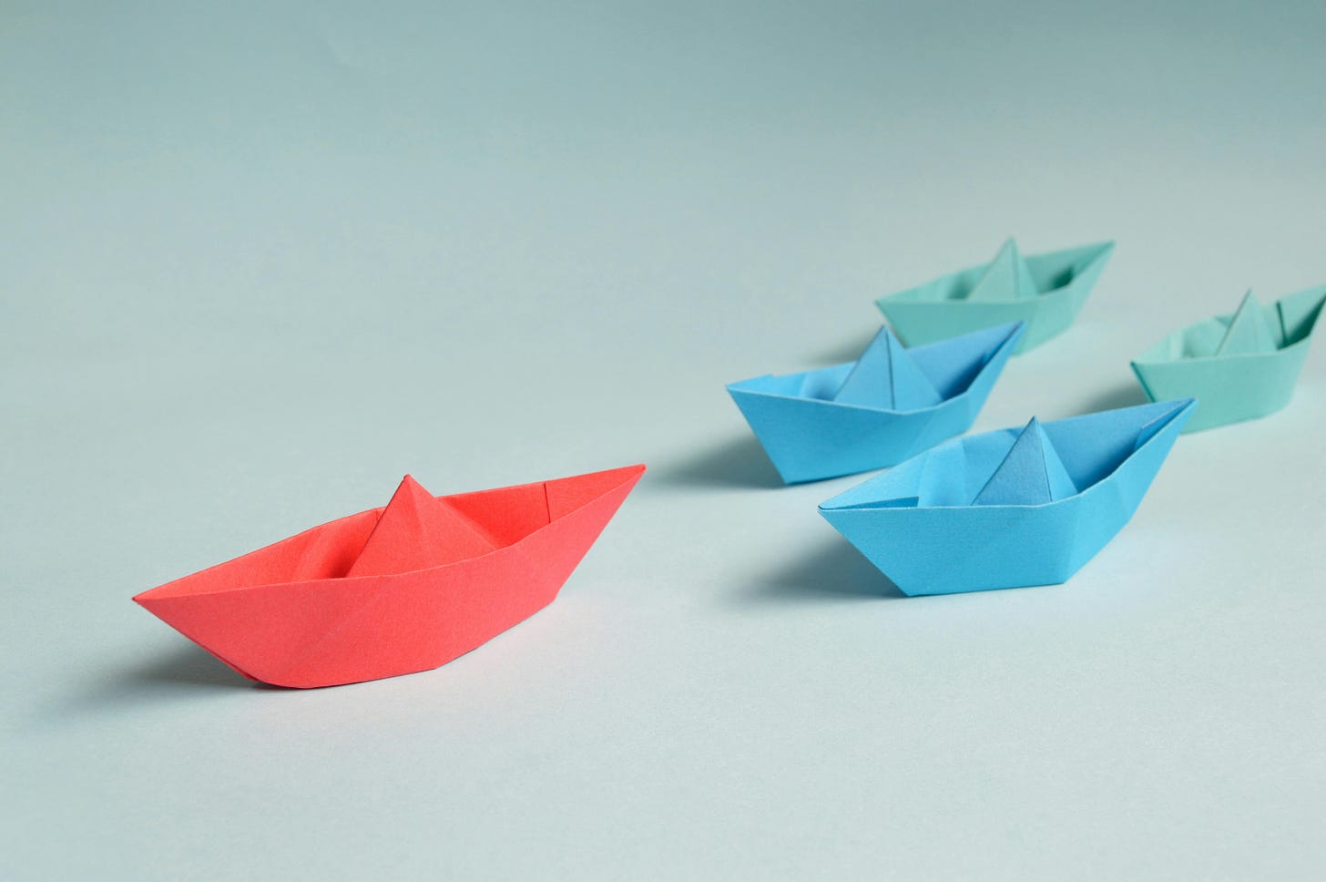 Little paper boats with one in red leading at the top