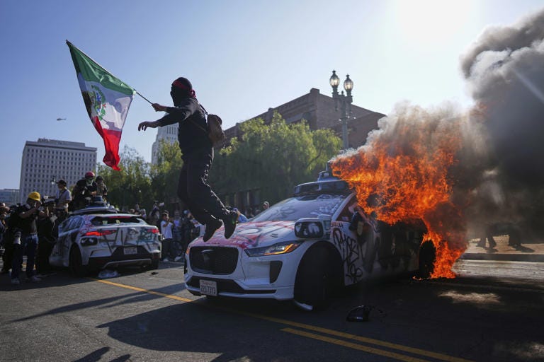 A protester leaps off a burning Waymo taxi near the Metropolitan Detention Center in downtown Los Angeles, Sunday, June 8, 2025, following immigration raid protests. Eric Thayer/AP Photo