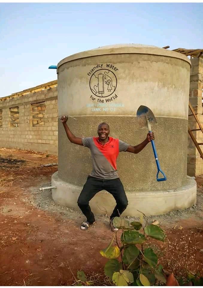 man posing in front of a water tank with Friendly Water logo on it