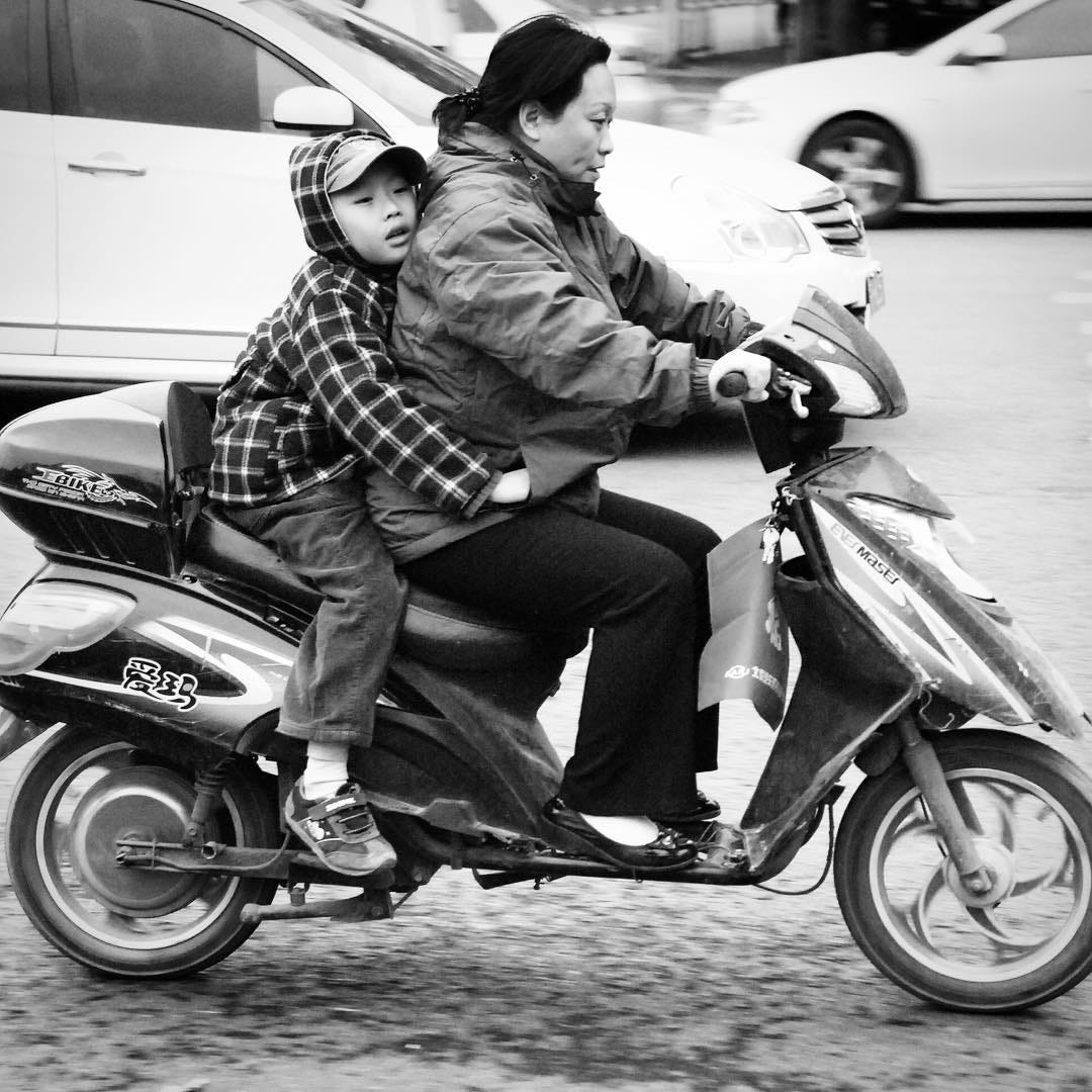 A woman rides an electric scooter with a child in the center of Beijing.