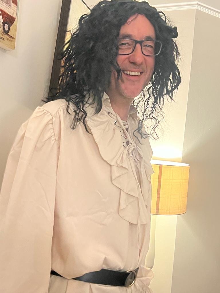 Simon Whaley, wearing a flouncy off-white pirate short and a long black wig