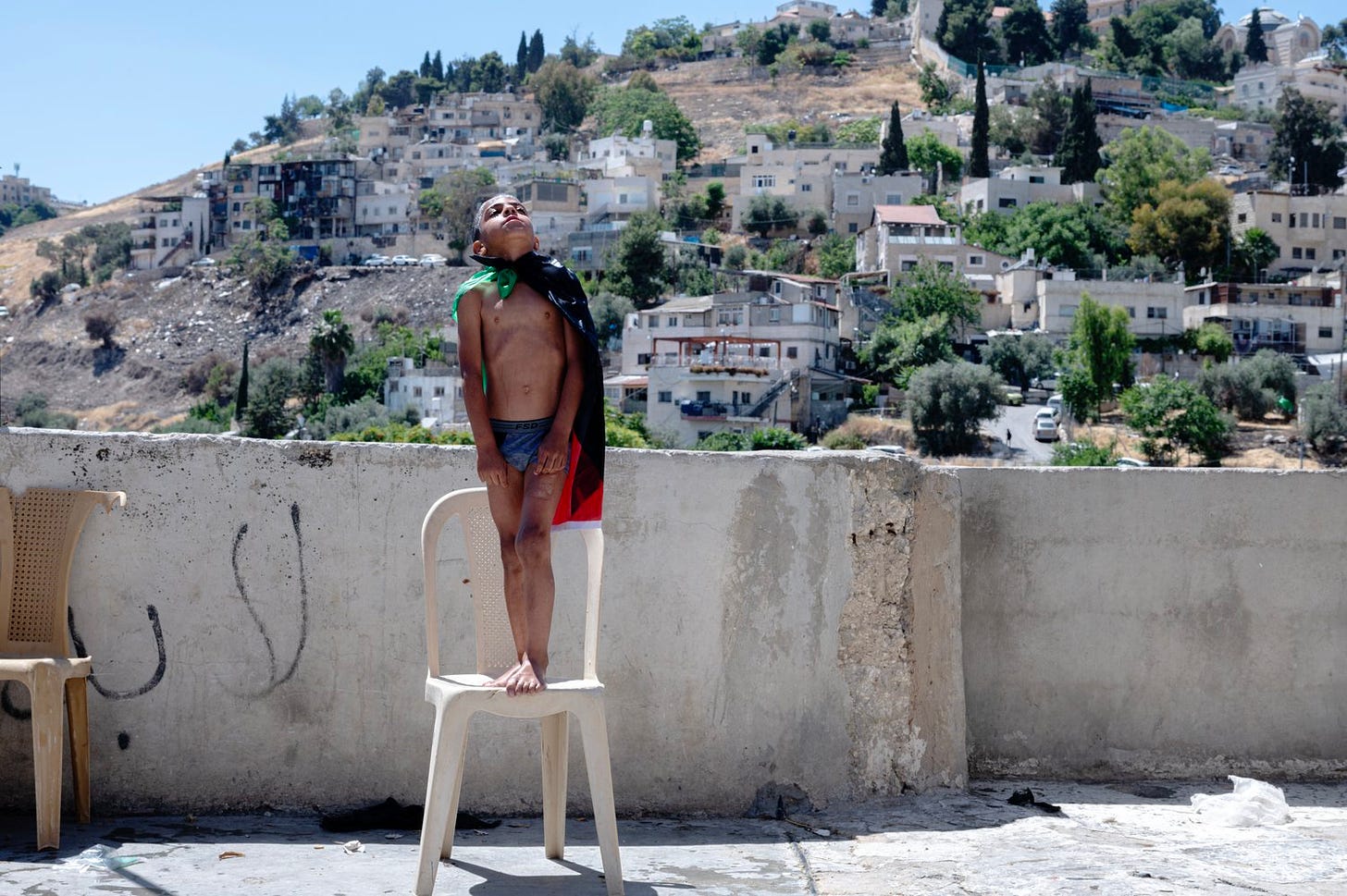 "Thaer al Rajabi, nine, wears a Palestinian flag as a cape while playing on the rooftop where his father, Kayed al Rajabi, set up an inflatable pool to make up for a missed vacation by the sea after Ramadan. “There was too much fear for us to leave our house,” says the 34-year-old father of eight. “So I brought them this pool.” The Palestinian family faces possible eviction from their home in the Silwan district of East Jerusalem because an Israeli settler organization sued, claiming the land had been owned by a Jewish trust more than a century ago. The United Nations estimates that 970 Palestinians in the city are threatened with eviction due to cases brought mainly by settler organizations."