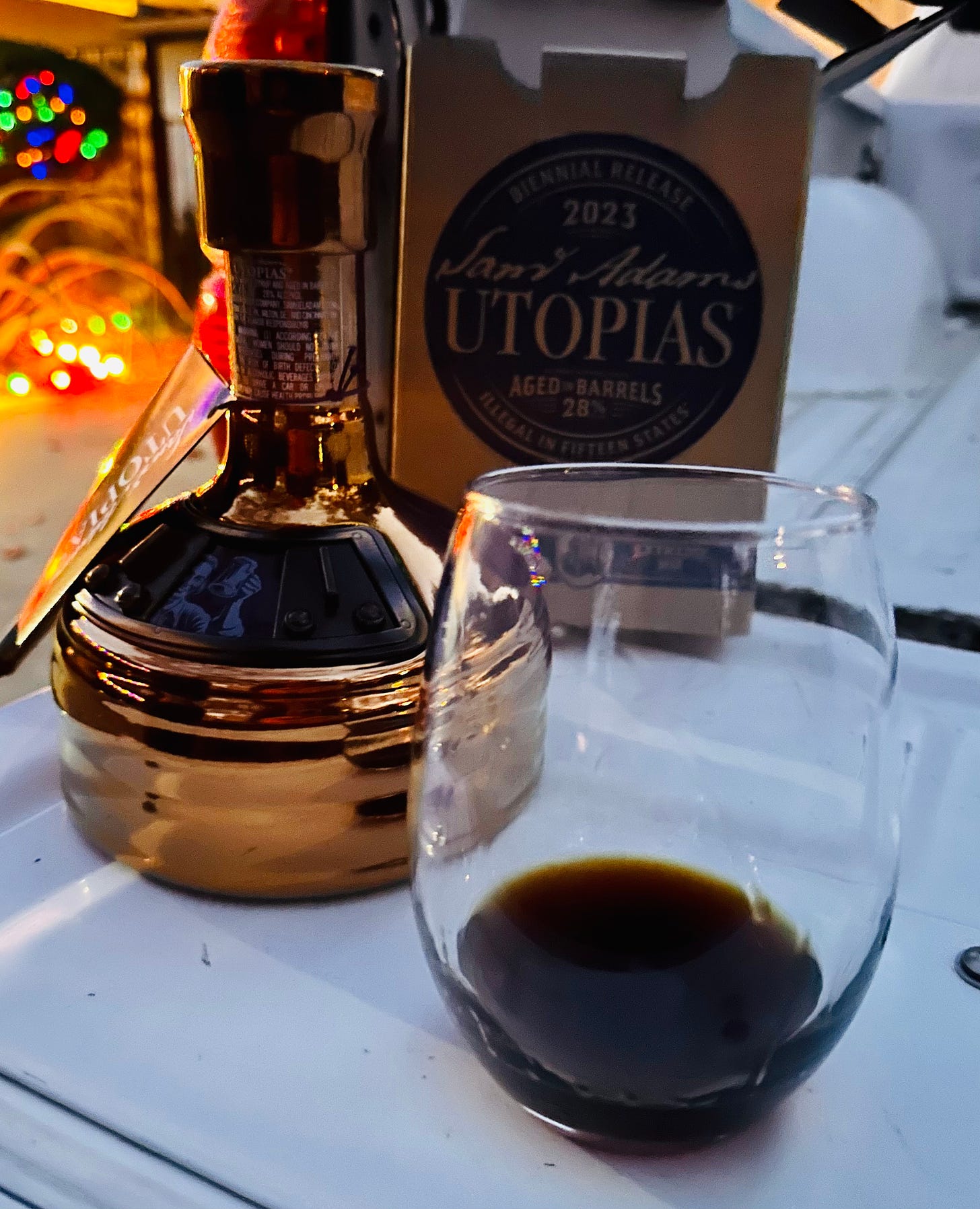 A bottle of Sam Adam's Untopias sitting next to a Utopias box and a glass of the beer sitting on a pickup truck tailgate