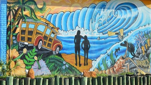 Mural on wall of Cocoa Beach building showing large wave and surfers standing and gazing at the wave.