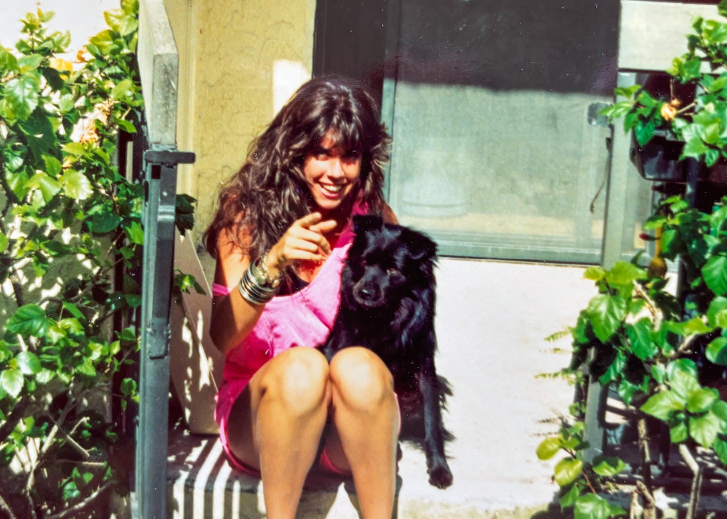 Young woman sitting on porch step with her arm around a black dog