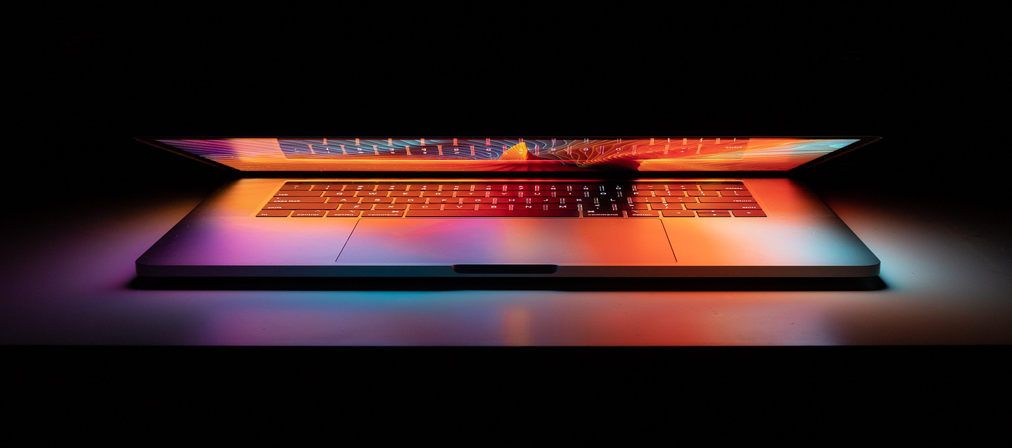 partly open laptop with glowing purple and orange screen, on a dark background
