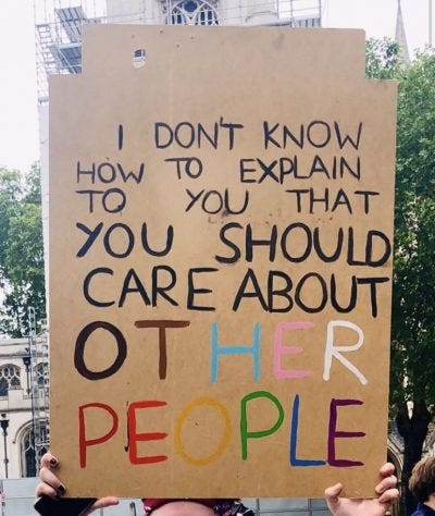 Photograph of a protest sign that reads: "I don't know how to explain to you that you should care about other people." The words "other people" are written in the colors of the progress pride flag.