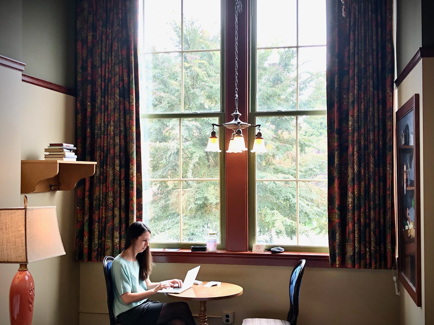 Photo of Nicole sitting at a table in a hotel room typing on a laptop.