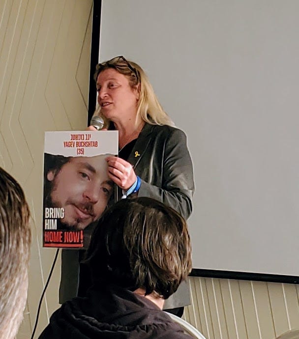 A woman with blond hair and a black jacket holds up a poster that reads Bring Him Home Now and over a photo of her nephew.