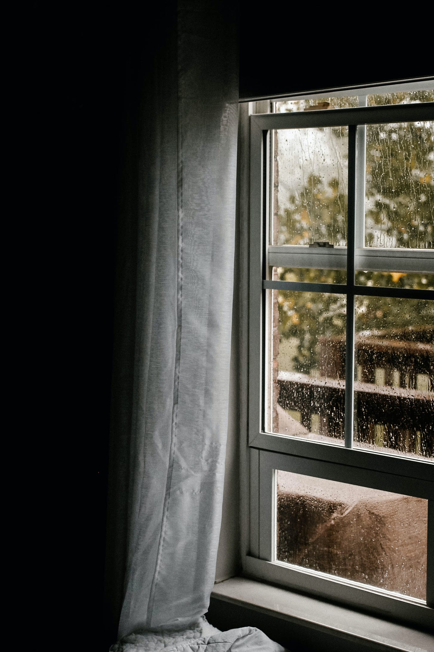 Inside a cozy house, rain run downs a window.