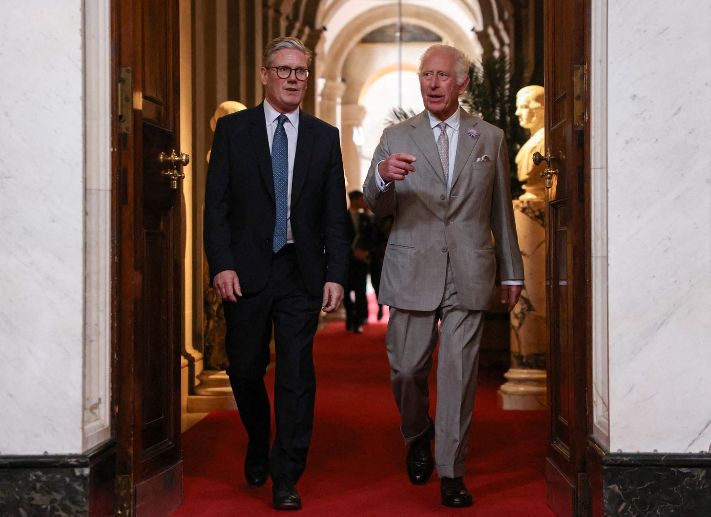 King Charles walking down a corridor with Keir Starmer