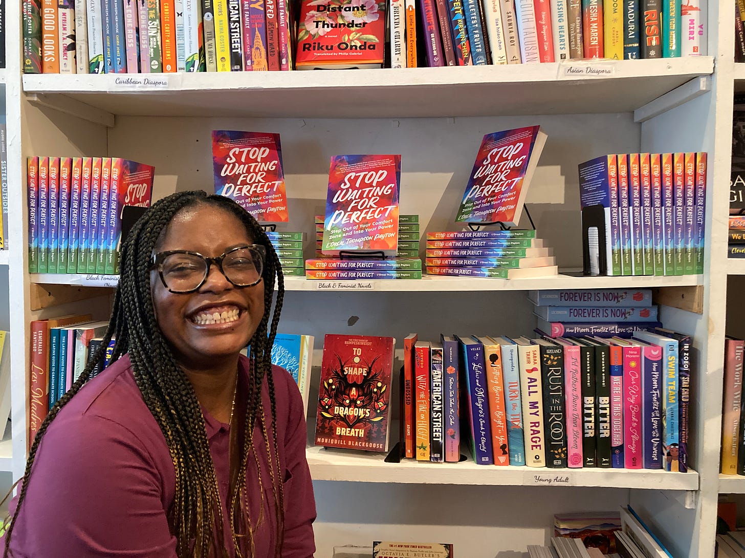 Picture of author L'Oreal Thompson Payton smiling in front of a display of her book, Stop Waiting for Perfect, at Brooklyn bookstore Café con Libros.