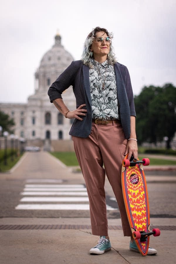 A woman holds a skateboard in front of a capitol building