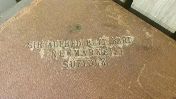 The top corner of the trunk, where someone has branded "Sir Alfred Butt Bart Newmarket Suffolk"