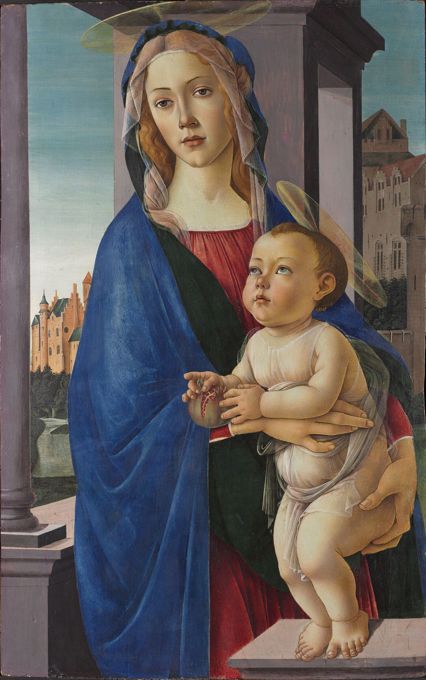 A woman holds a baby in front of a background of buildings.