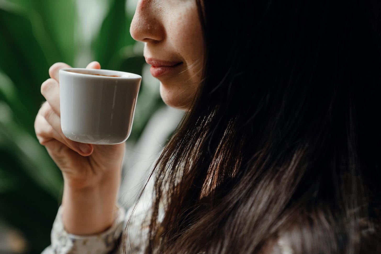A woman holds a white cup of coffee to her lips.