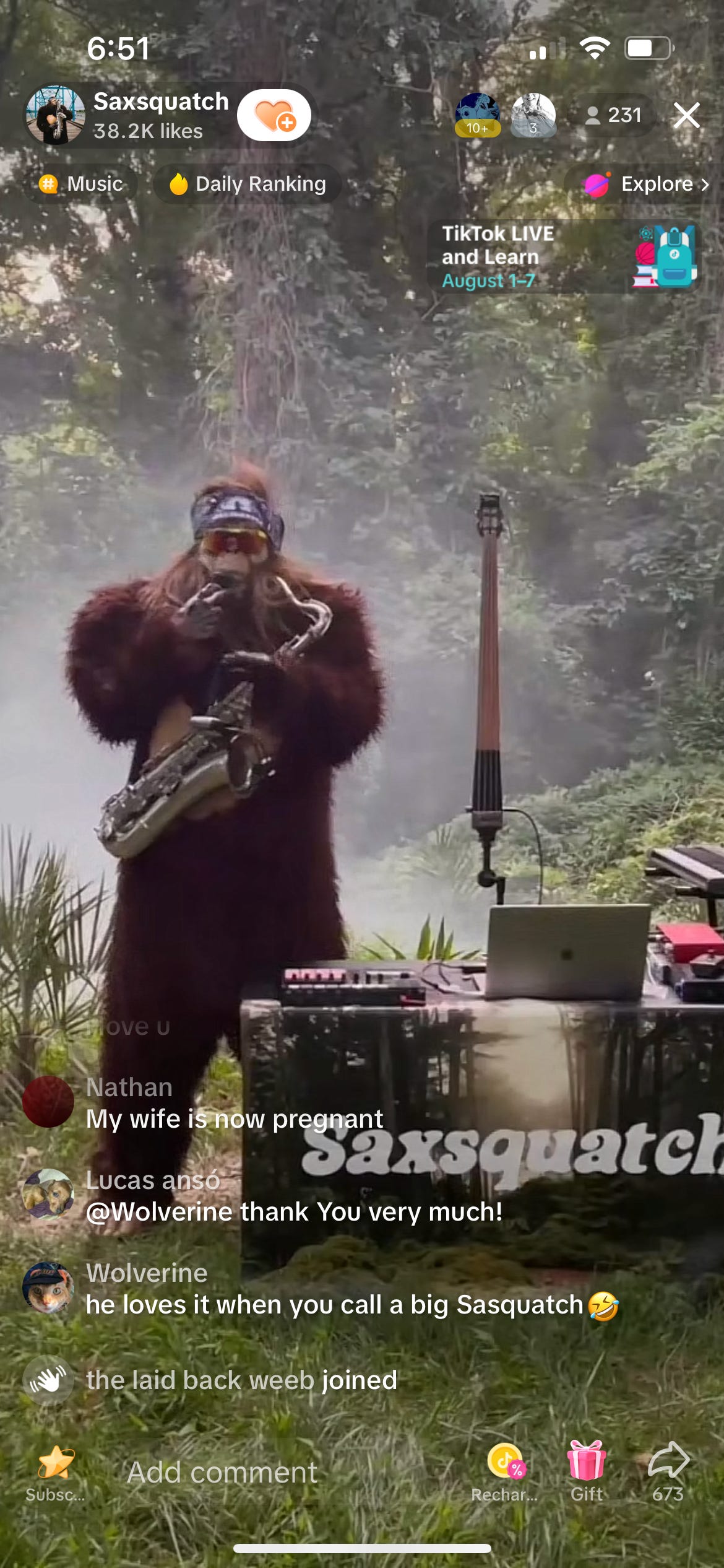 TikTok screenshot of a guy in a sasquatch costume in the forest standing next to a table with some DJ equipment and playing the sax.