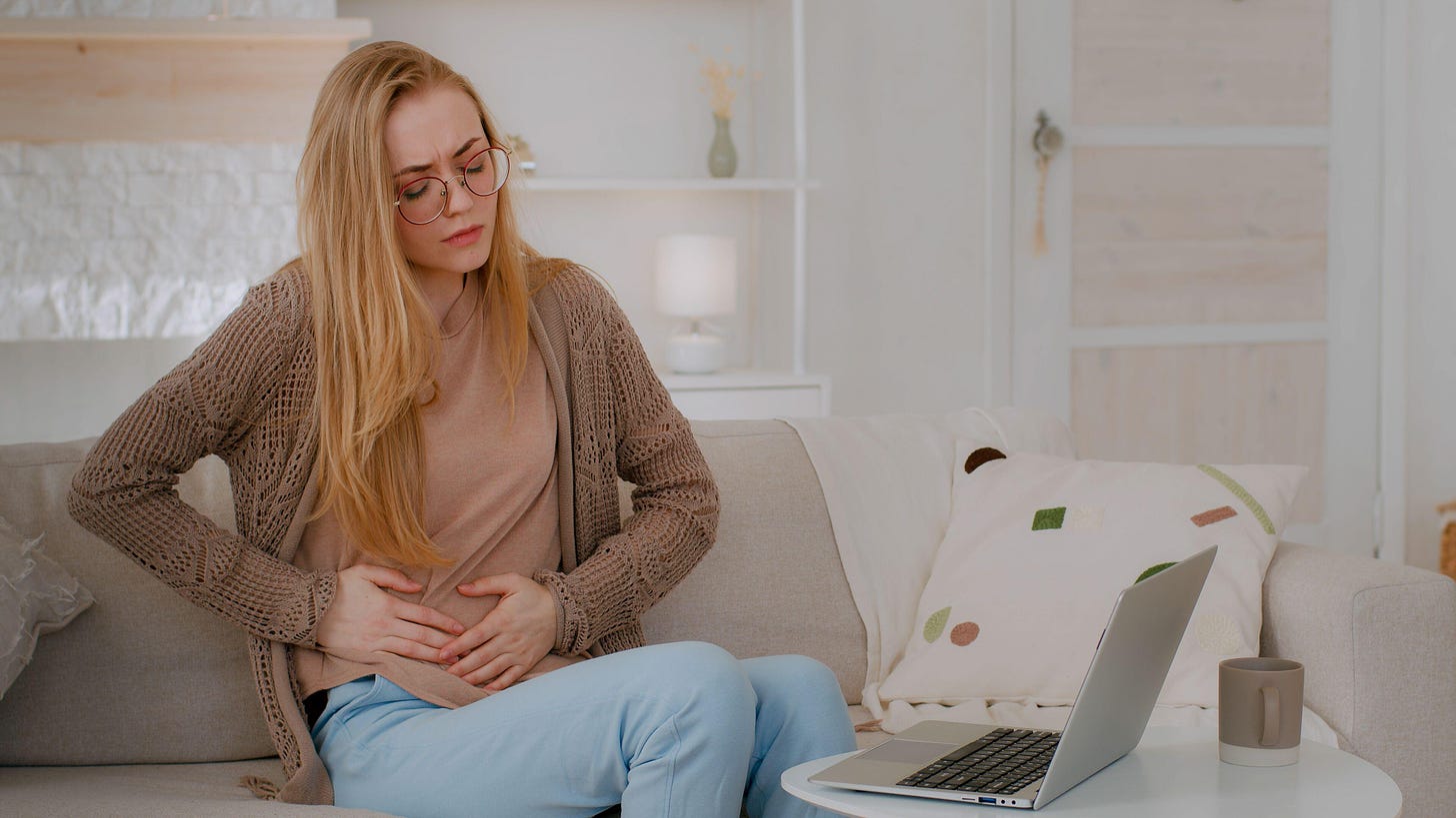 Young woman sat on a sofa experiencing cramps 