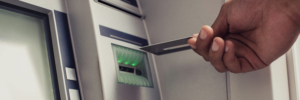 A hand inserting a debit card into an ATM