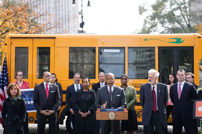 Mayor Eric Adams and other officials speak in front of an electric school bus.