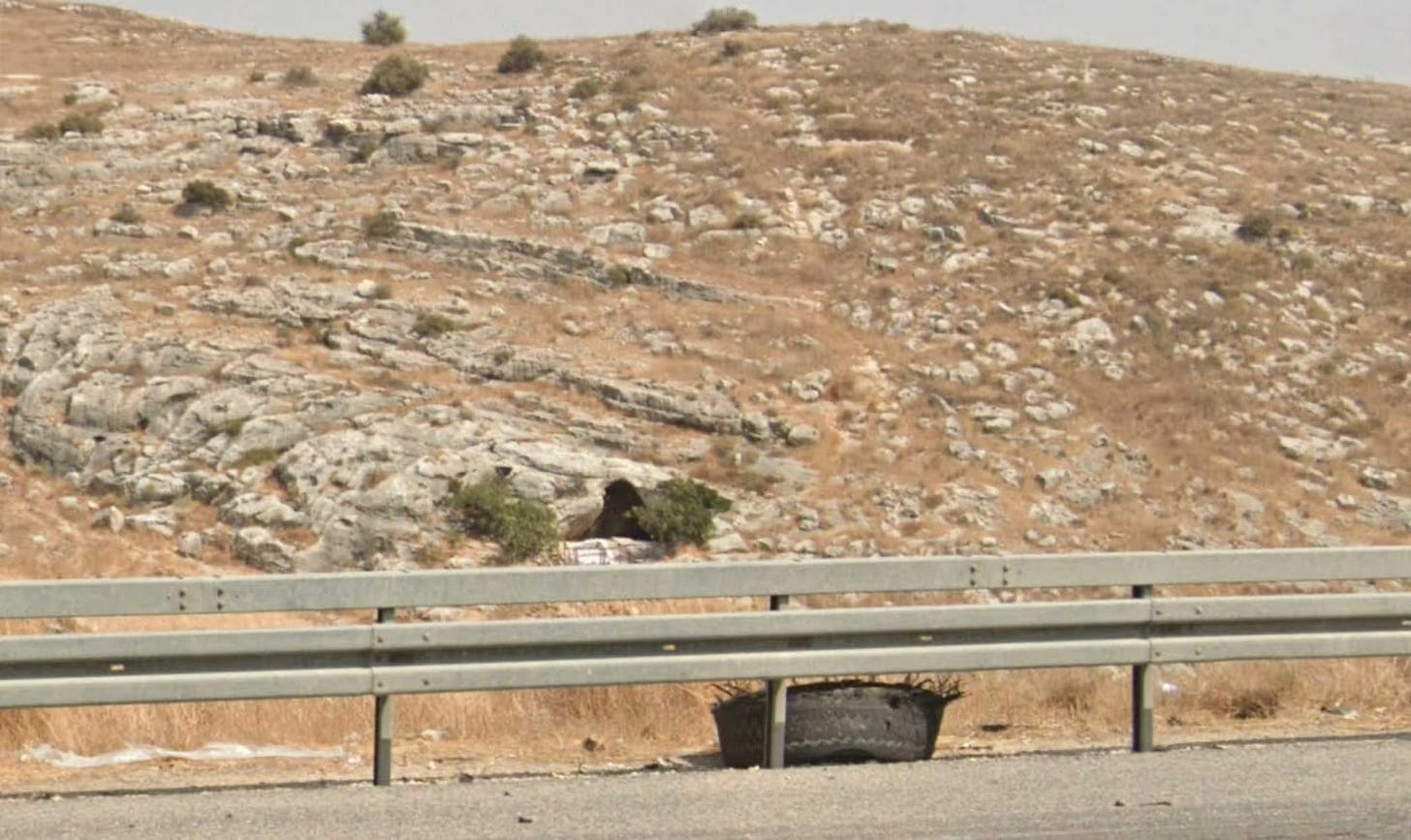 Small cave in a limestone hillside with a guardrail and highway in foreground