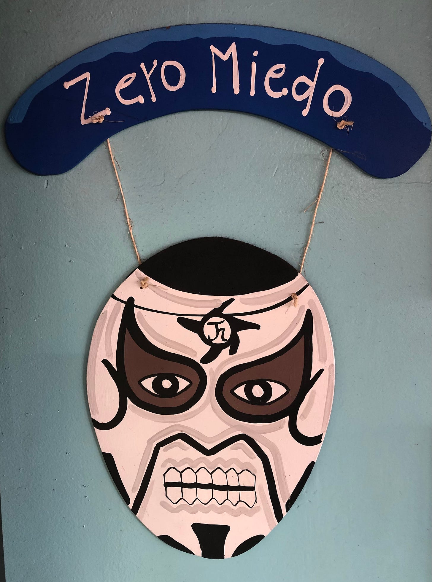 A sign saying ‘zero miedo’ and having the face mask of a luchador in pink, brown, and black.