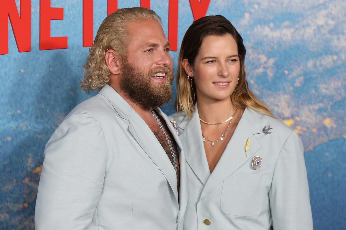 A picture of Jonah Hill and Sarah Brady wearing matching gray blazers in front of a Netflix banner.