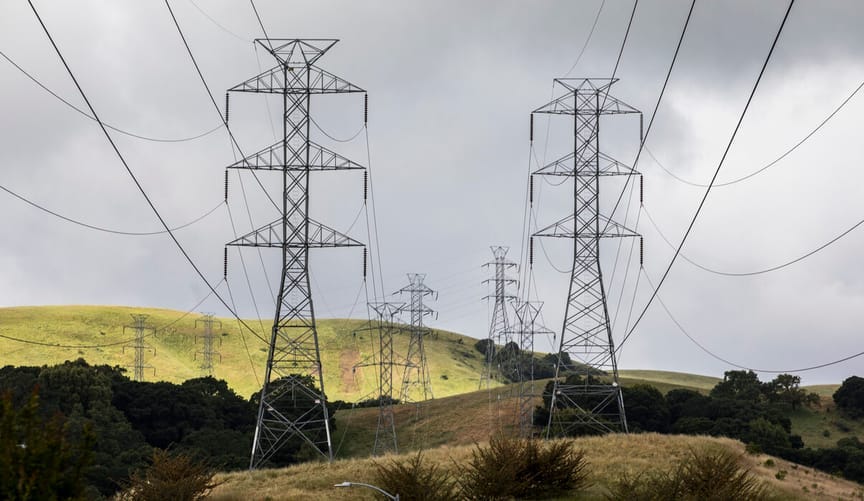 large transmission towers and wires are string across a green, hilly valley