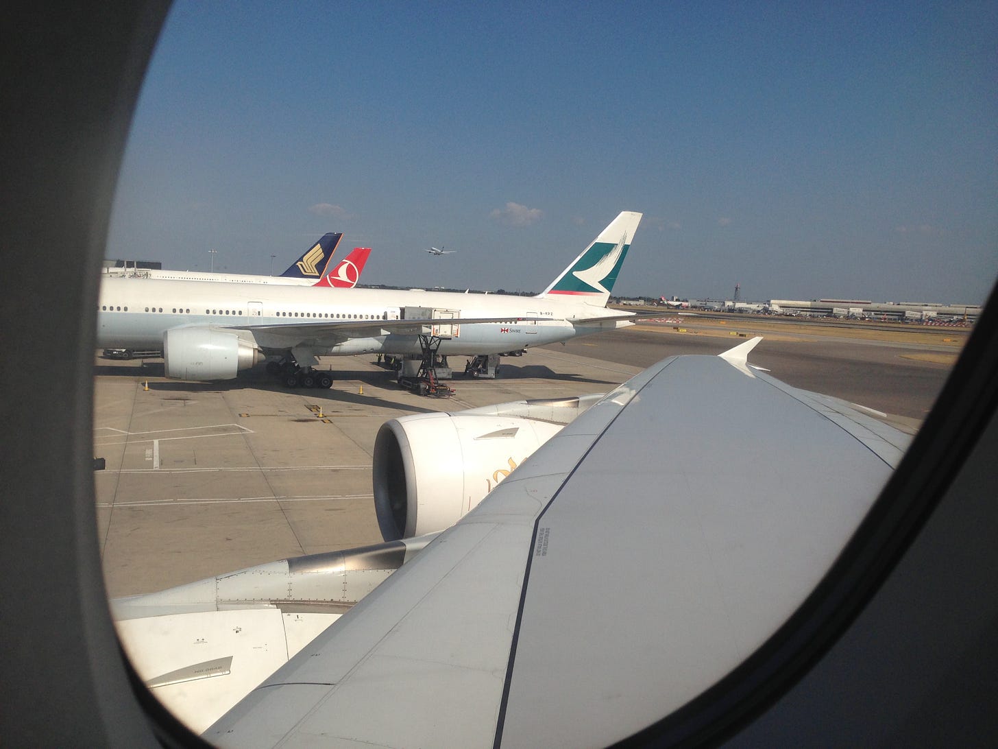 View from an aircraft window while still at the gate showing the wing, engine and other aircraft in the distance