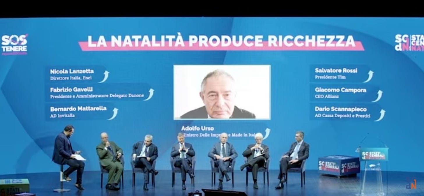 Nell'immagine si vedono 8 uomini sul palco. Il titolo dell'incontro è "La natalità produce ricchezza"