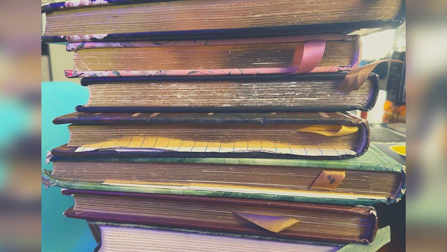 Seven well loved and worn in journals stacked on top of one another.