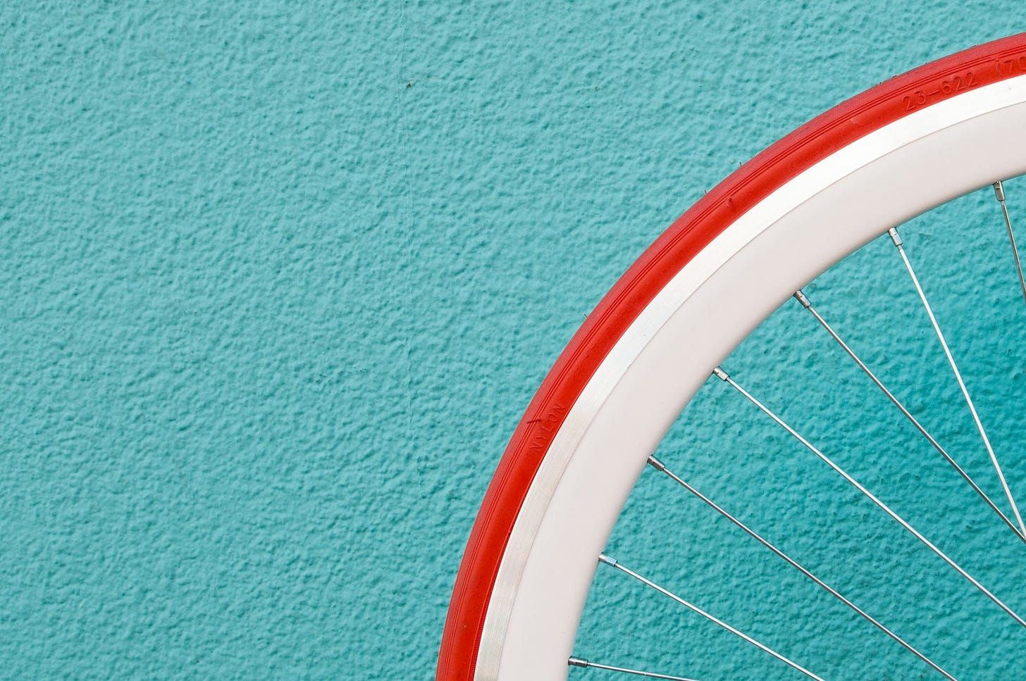 Muro azzurro acqua con in primo piano, sulla destra, un quarto di copertone di una bici: copertone rosso all'esterno e bianco all'interno.