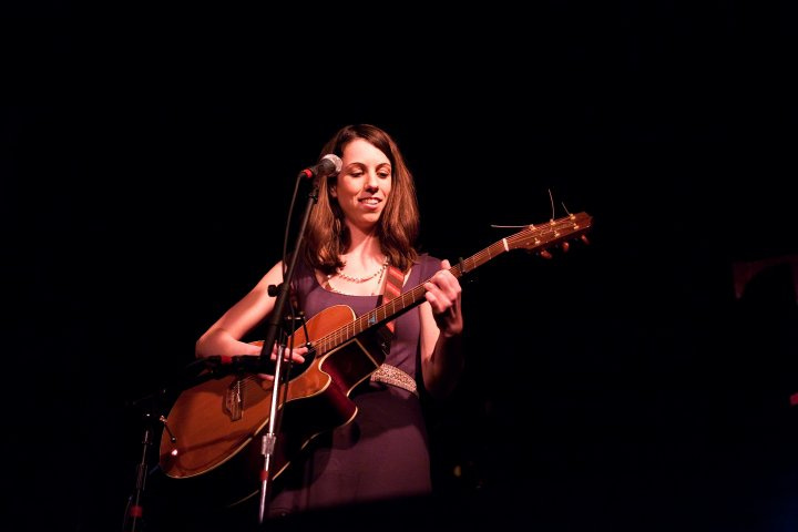 Photo of Nicole performing on stage with a guitar and microphone