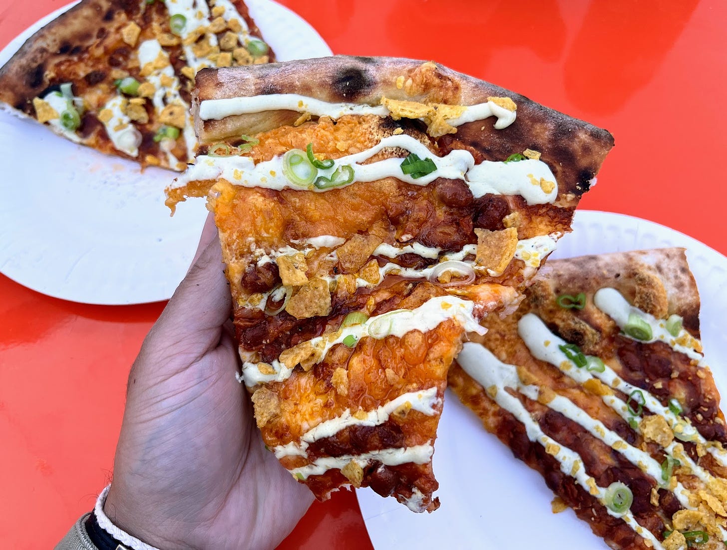 Hand holding half eaten The Questing Taco pizza