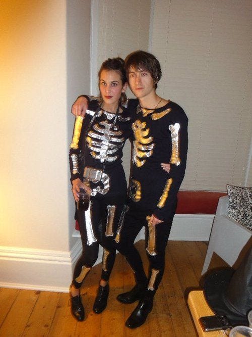 Alex Turner e Alexa Chung com uma fantasia de esqueleto (macacão preto de mangas compridas com os "ossos" bordados em prateado)