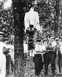 Leo Frank's corpse hanging from a tree after the lynching. His hands and feet bound. A crowd of spectators surrounds the tree. Leo Frank's corpse hanging from a tree after the lynching. His hands and feet bound. A crowd of spectators surrounds the tree.