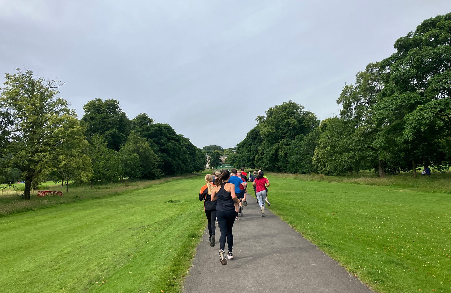 Runners on a wide path bordered by short grass which slopes away on either side
