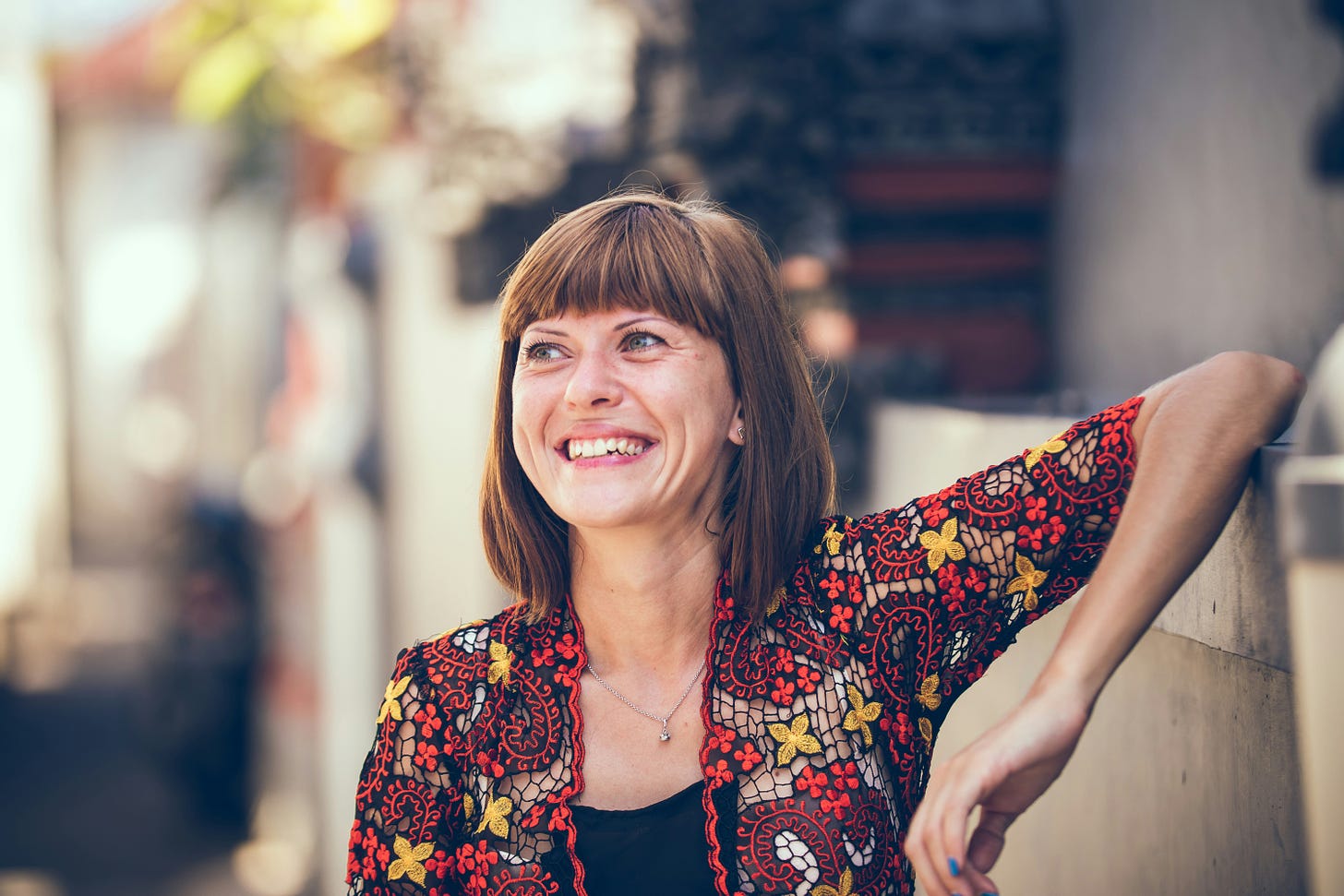 middle age woman in a red and yellow floral jacket leaning up against a wall and looking up and to the left