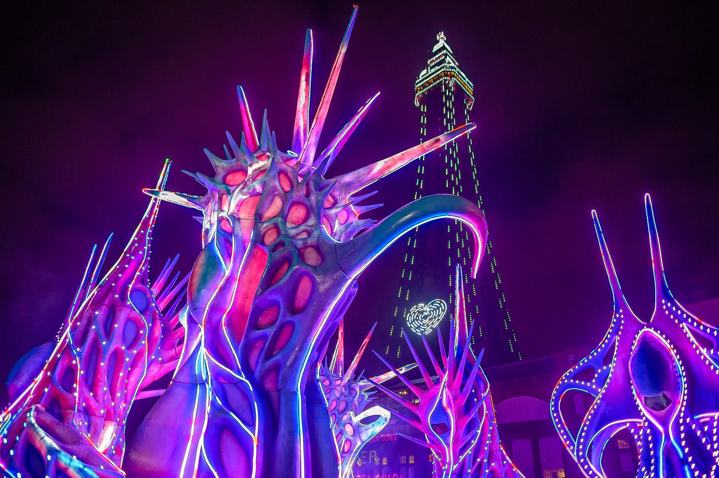 Large monstrous creations are illuminated in purple colours against the backdrop of Blackpool Tower.