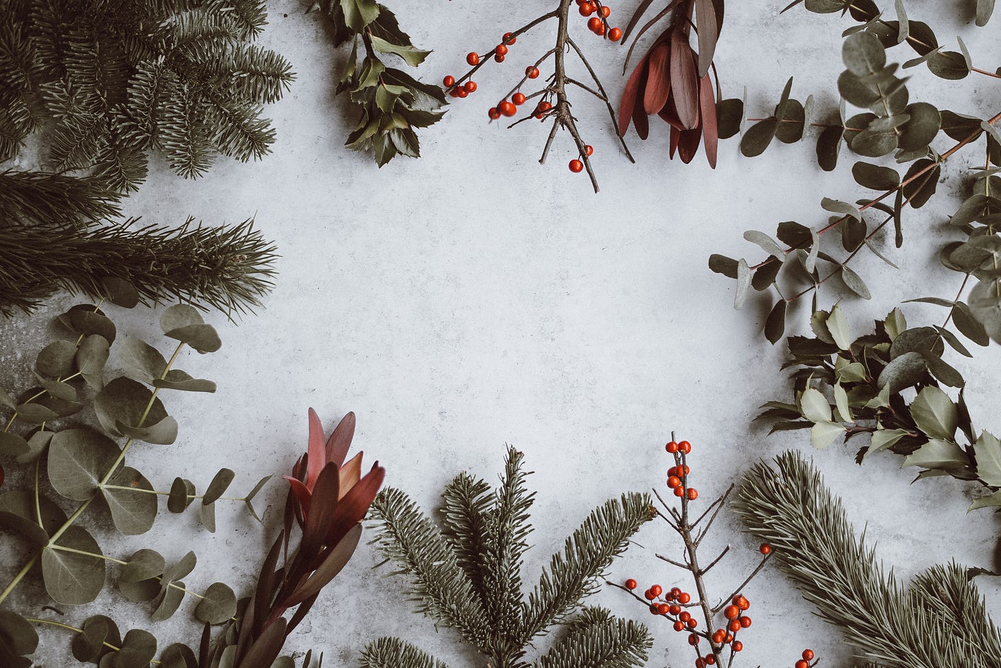 A flatlay, Christmas themed, with twigs, holly and red berries laid out on a white background 