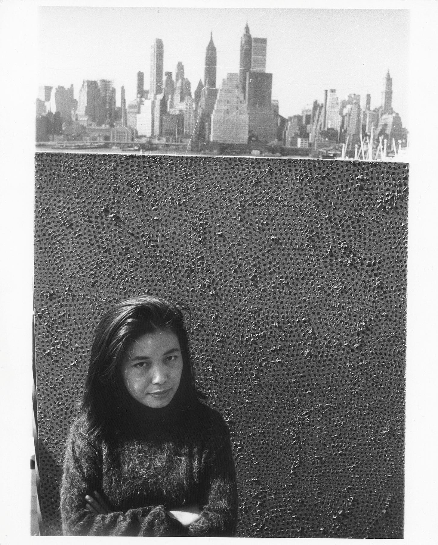 Kusama stands in front of an infinity net painting with New York's skyline behind her