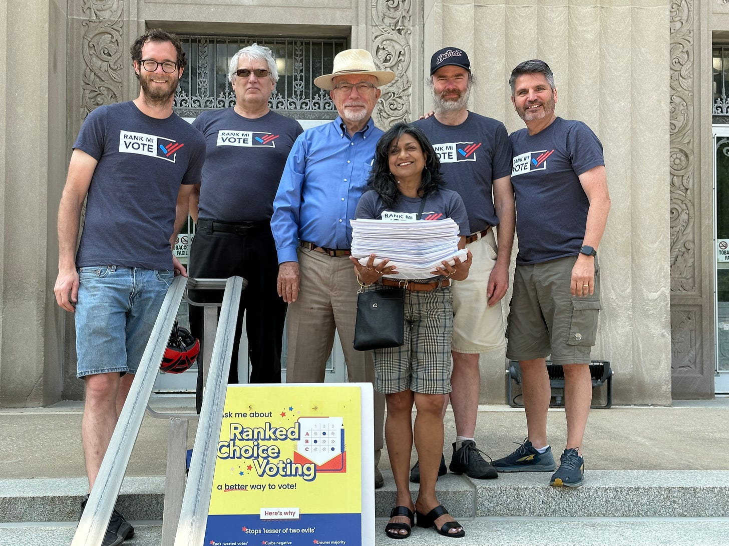 Rank MI Vote volunteers in front of Kalamazoo City Hall on Wednesday, May 24, 2023, before submitting 520 initiative petition sheets to the City Clerk's office.  Pictured (L to R) are Justin Barney, Paul Vanryswyk, Jack Urban, Christina Dorett, Jeff Messer, and Ron Zimmerman.  Photograph taken by WMU Political Science Chair John Clark.