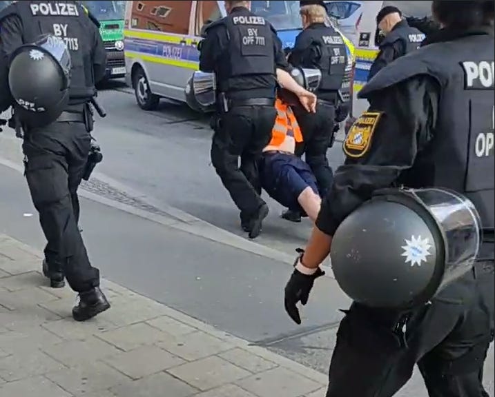 Simon Lachner wird von zwei Polizisten weggeschleift, im Vordergrund weitere Polizisten, im Hintergrund Polizeifahrzeuge