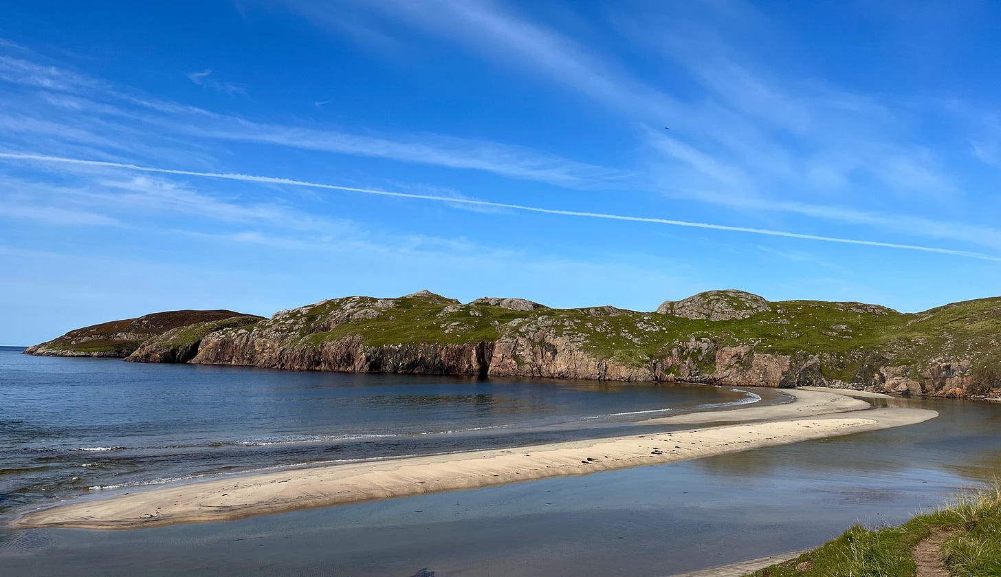 rocky cliffs topped with mossy green grass. pink sand spit, and dark blue sea