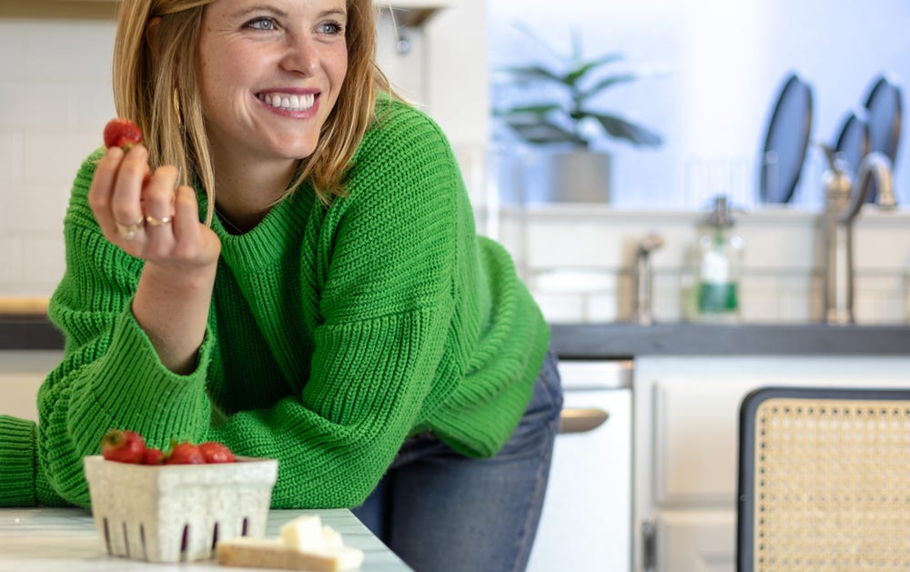 Anja with elbows on table smiling holding a strawberry