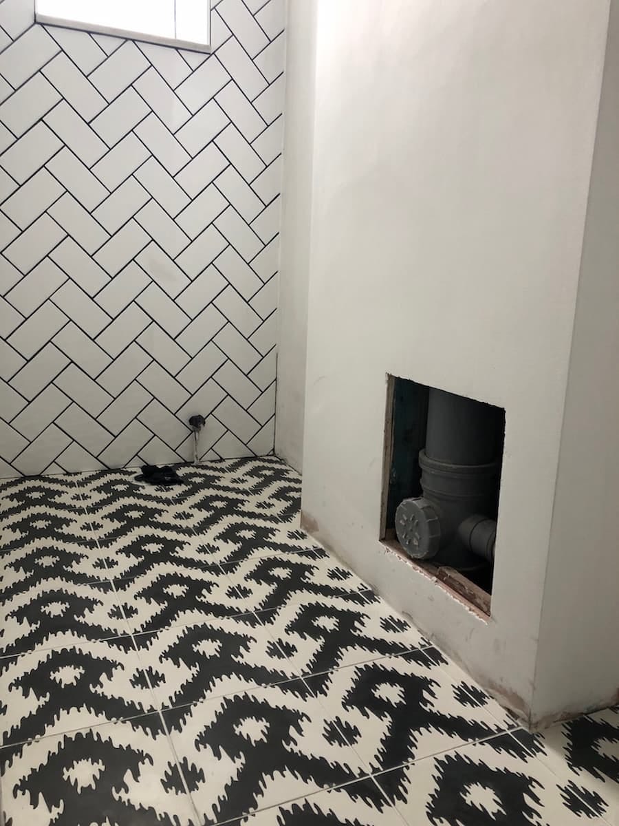 Black and white tiled bathroom floor and wall. The floor has a black and white zigzag pattern. The wall has a black and white herringbone pattern using white metro tiles and black grout. 