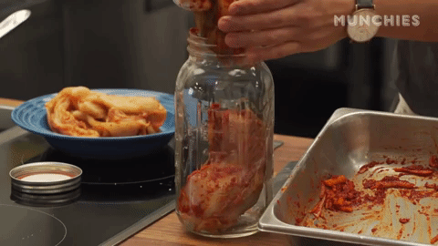 A person's hand stuffs red-coated cabbage leaves into a jar.